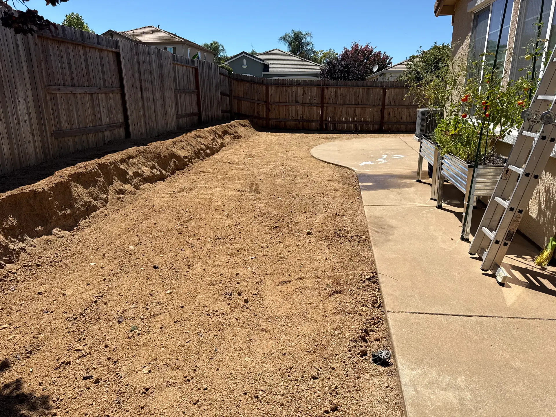 Prepared backyard soil and excavation beside a concrete patio